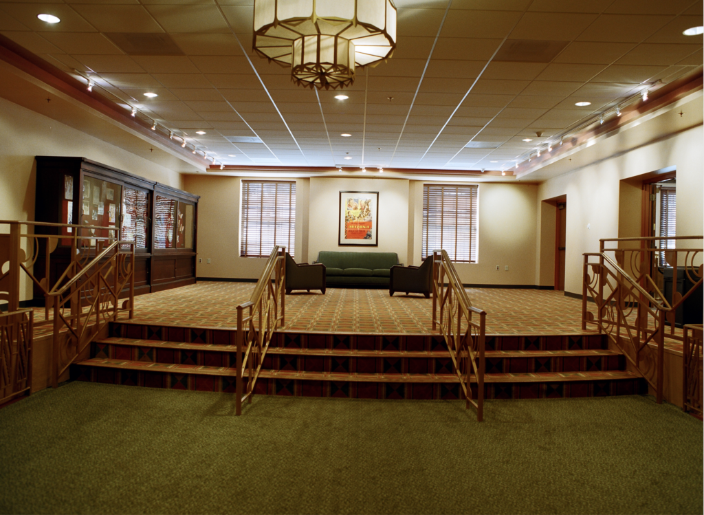 interior shot of the lobby it is showing a long staircase with only three stairs leading up to a small sitting area. It is very antique and historic looking from the carpet to the handrails to the chandeliers.